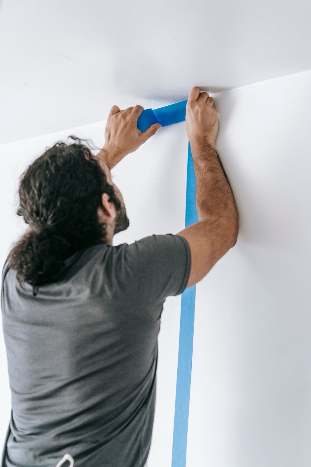 Close-up of a decorator pressing masking tape along a freshly cut paint edge