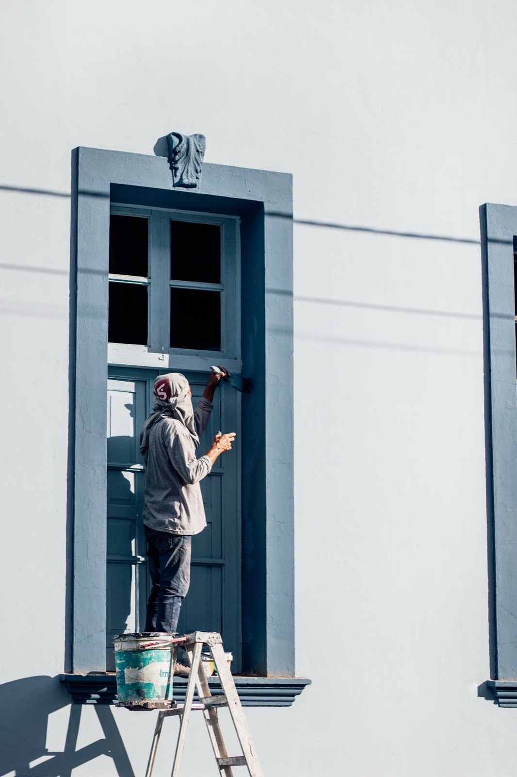 A decorator on a ladder painting a window frame on a house exterior