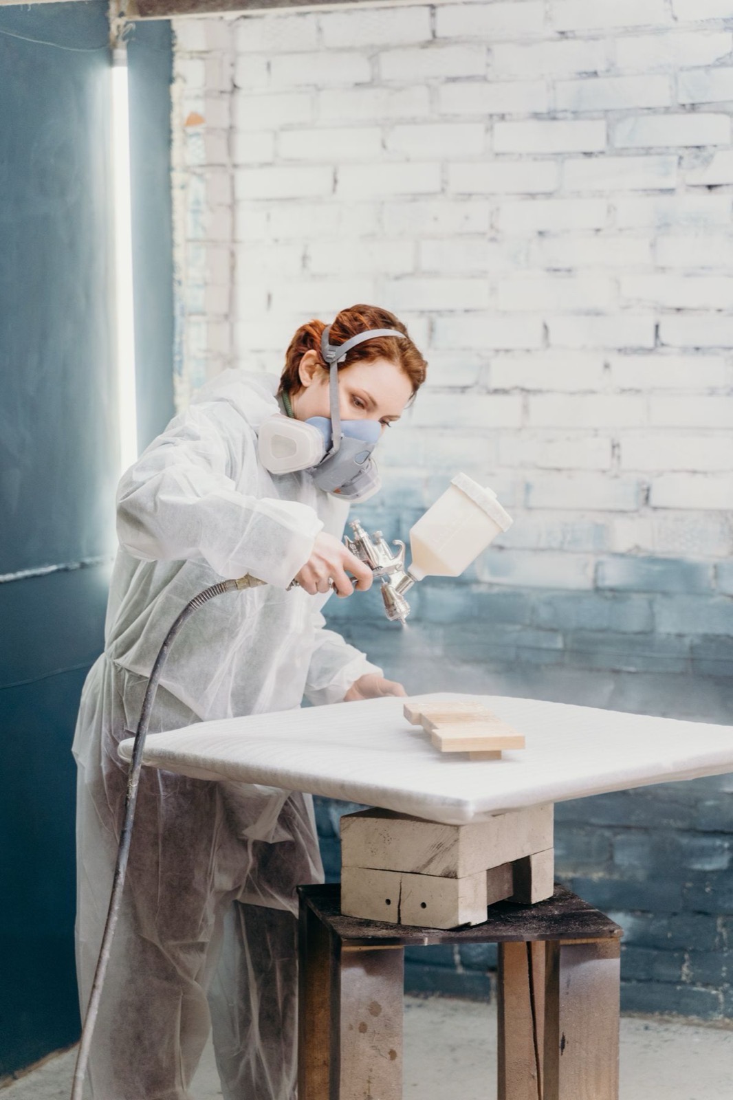 A decorator in full PPE spraying an even coat of paint onto a wooden panel